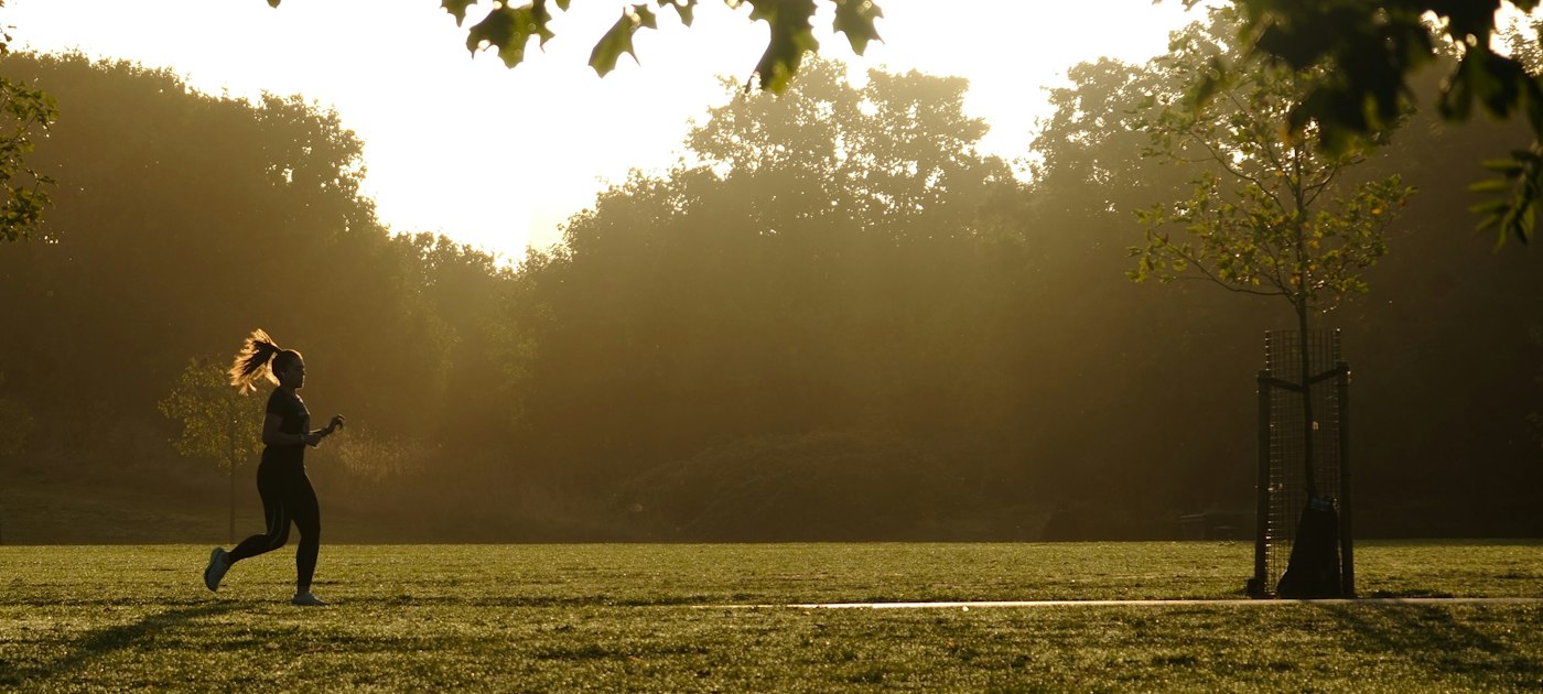A runner moving through a park in warm evening light